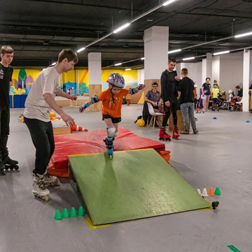 Дети учатся кататься на роликах на специальной площадке в помещении