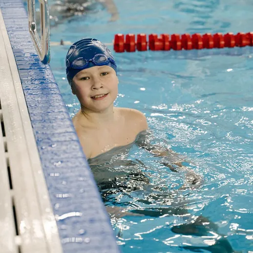 Мальчик в купальном костюме улыбается после тренировки в бассейне на спортивных соревнованиях