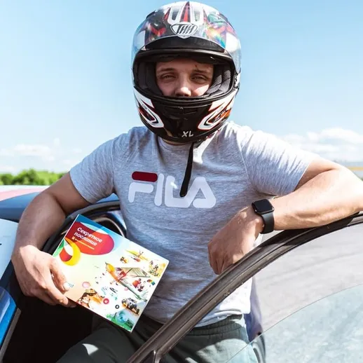 Гонщик на треке с книгой о гонках в руке на фоне ясного неба