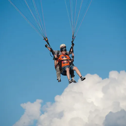 Парашютист опускается к земле над белыми облаками в ясный день