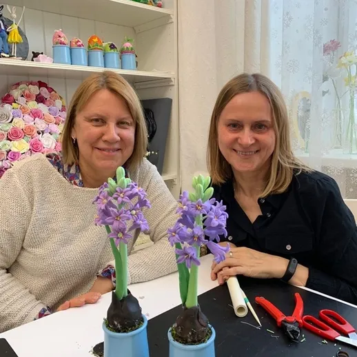 Две женщины за столом занимаются цветами в мастерской на уютном светлом фоне