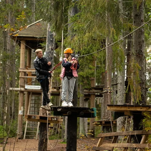 Два человека на канатной дороге в лесу, наслаждаясь активным отдыхом с друзьями в осенний день