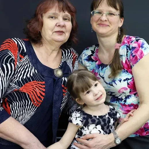 Три поколения женщин радостно позируют вместе в помещении с нейтральным фоном