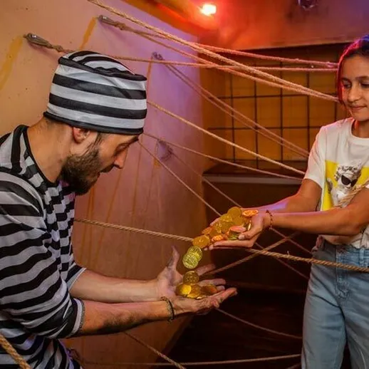 Девочка передает золотые монеты человеку, связанному веревками, в комнате с яркой подсветкой