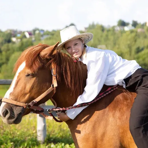 Девушка обнимает лошадь на фоне зеленых полей и деревьев в солнечный день