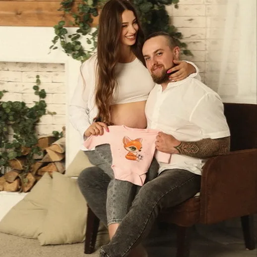 Счастливая семья готовится к появлению малыша в уютном доме с милым детским комбинезоном