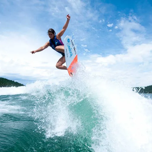 Серфингист ловит волну на солнечном пляже летом, поднимаясь в воздух над водой в красивом природном окружении