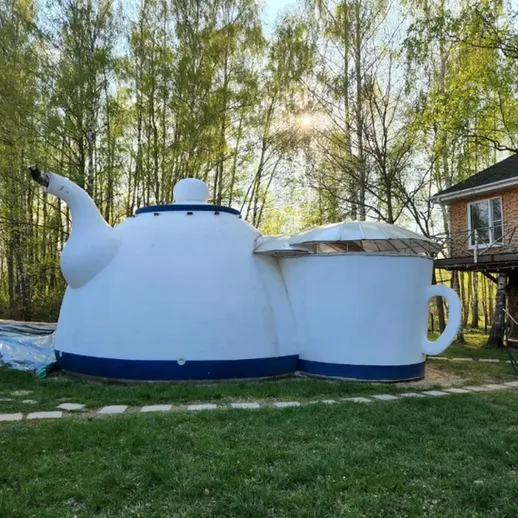 Огромный чайник в зеленом саду рядом с домом на фоне весенних деревьев