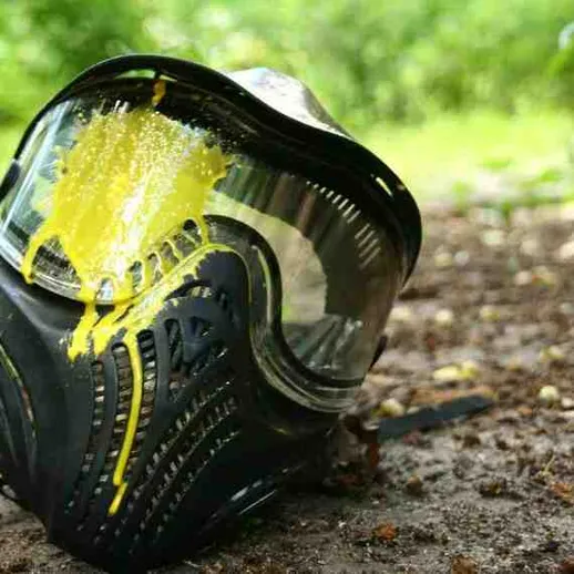 Маска для пейнтбола с желтой краской на земле в лесу после игры на свежем воздухе в солнечный день