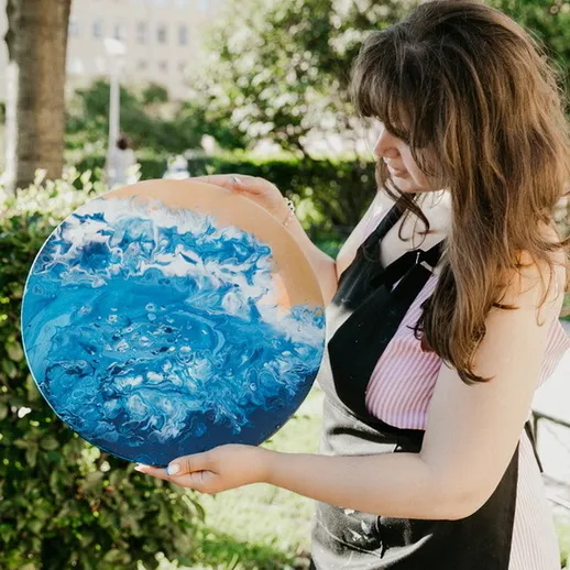 Художница показывает готовую работу с абстрактным морским пейзажем на улице в солнечный день