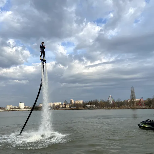 Человек, используя флайборд, поднимается над рекой в ясный день