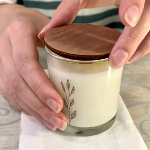 Женщина закрывает ароматическую свечу деревянной крышкой на столе в уютной обстановке