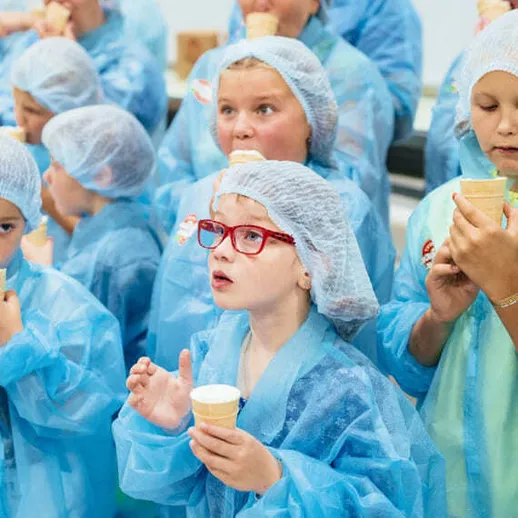Дети в защитной одежде вкушают мороженое на экскурсии в фабрике в летний день