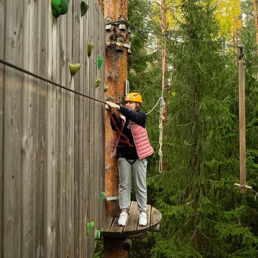 Девочка занимается скалолазанием на тренировочной стенке в лесу в солнечный день