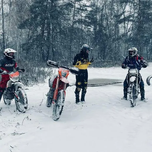 Группа мотоциклистов на зимней трассе в лесу, занимающихся эндуро в снежную погоду