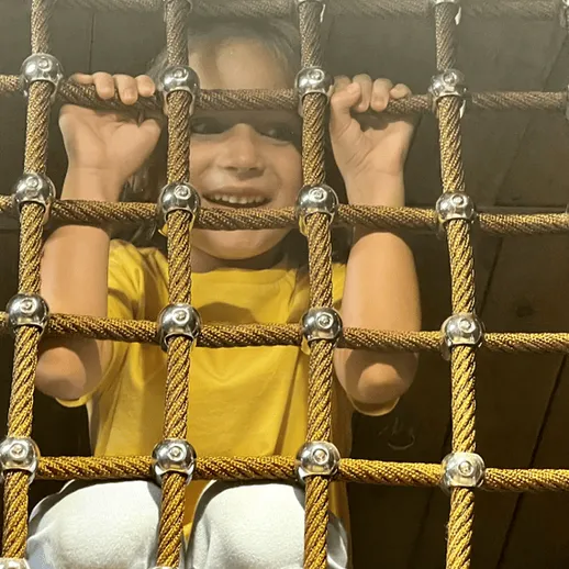 Ребёнок играет на игровой площадке, проходя через сетку в закрытом пространстве