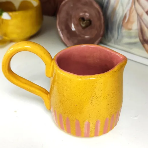 Керамическая жёлтая соусница с розовыми полосами на фоне домашнего интерьера