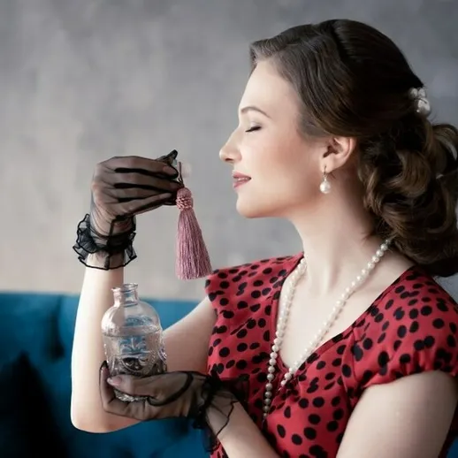 Женщина в красном платье с горохами, наслаждающаяся ароматом флакона на фоне синего дивана