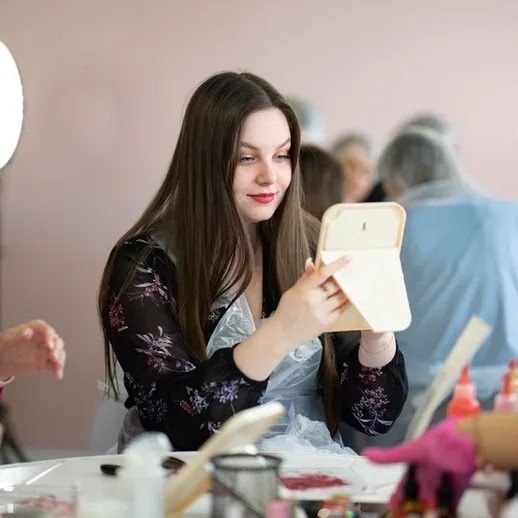 Девушка за столом с зеркалом на фоне мастеров по макияжу в косметической студии