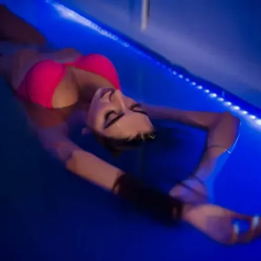 Девушка в розовом купальнике распускает волосы в синем бассейне в вечернее время