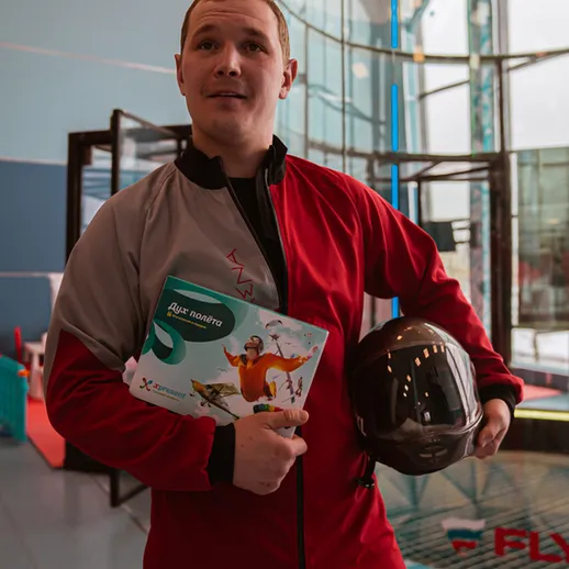 Мужчина в защитном костюме и шлеме готовится к полету в аэродинамической трубе в спортивном центре