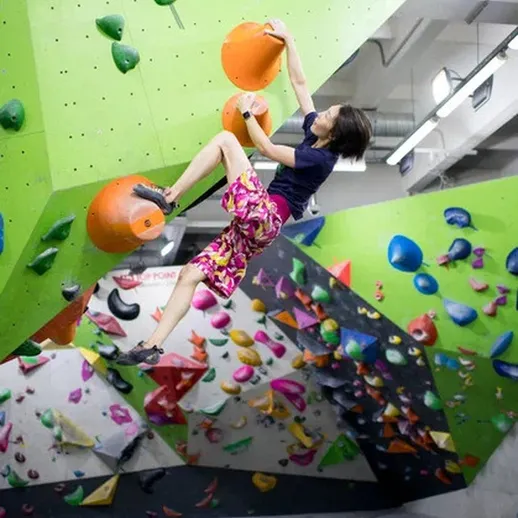 Спортсменка занимается скалолазанием на тренировочной стене в спортивном зале