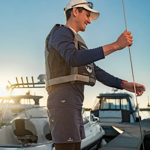 Мужчина на причале ловит рыбу на закате, морской пейзаж и яхты вокруг