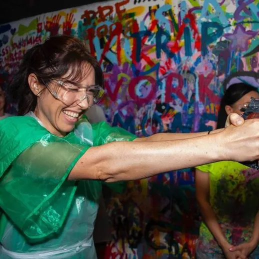 Женщина стреляющая из пистолета в арт-студии с яркими граффити на стенах