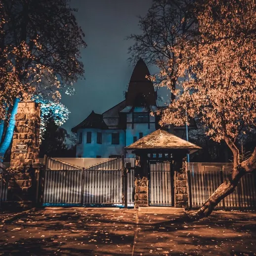 Ночной взгляд на старинный особняк с запертой воротами и деревьями в освещении луны