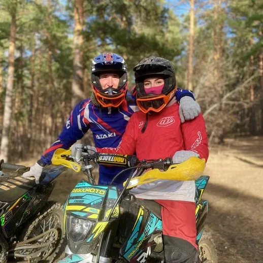 Два мотоциклиста на мототрахе в лесу, улыбаются и позируют на фоне деревьев в солнечный день