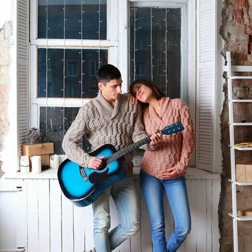 Молодая пара играет на гитаре в уютной комнате с большим окном