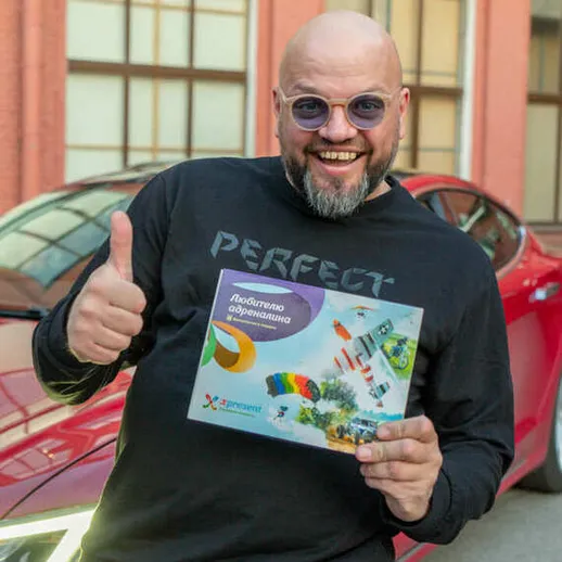 Улыбающийся мужчина позирует с буклетом на фоне красного автомобиля в солнечный день