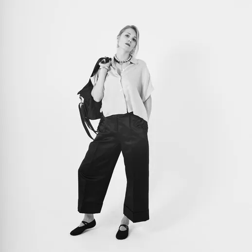 Молодая женщина стоит на белом фоне с сумкой через плечо и модным нарядом в светлом и темном цветах