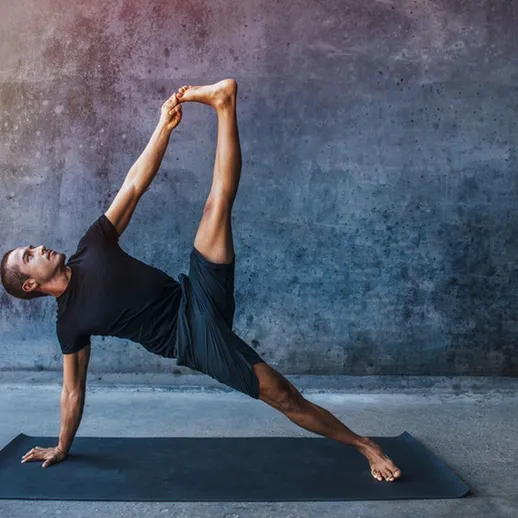Йога у стенки в студии с хорошим освещением, мужчина выполняет сложную асану в утренние часы