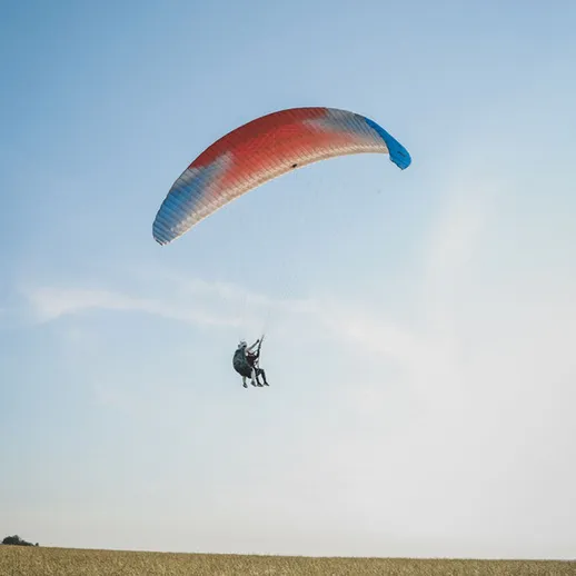 Парапланерист под ярким небом над зелёным полем, наслаждающийся свободным полётом в солнечный день