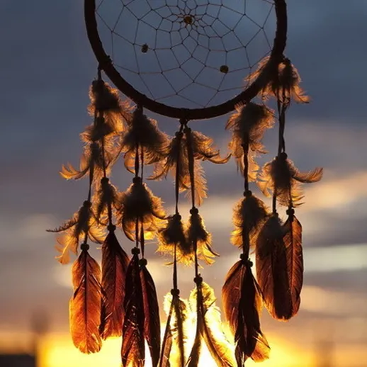 Ловец снов с перьями на фоне заката в небесах, создающий атмосферу спокойствия и гармонии в природном окружении