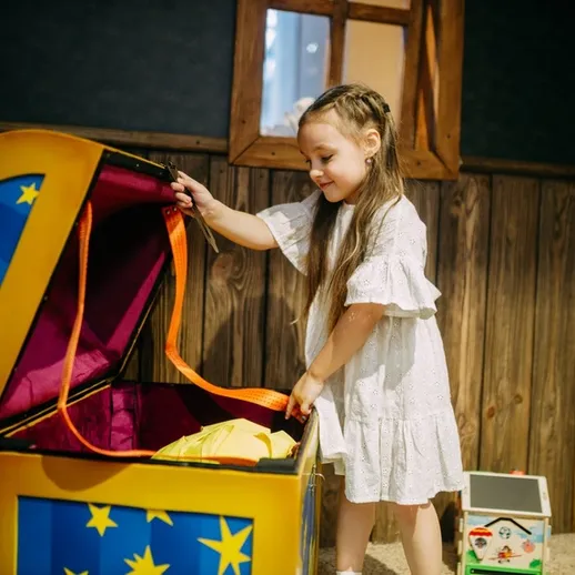 Девочка открывает яркий сундук с игрушками в игровой комнате