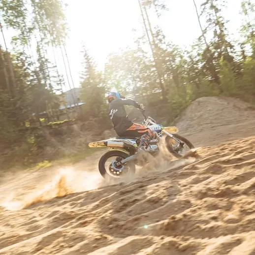 Мотоциклист осуществляет трюки на песчаном поле в лесу при ярком солнечном свете