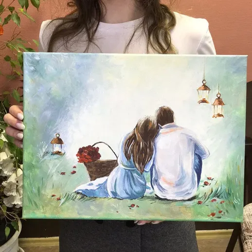 Пара, сидящая на траве, любуется красочной картиной с фонариками и корзиной цветов в романтичной обстановке