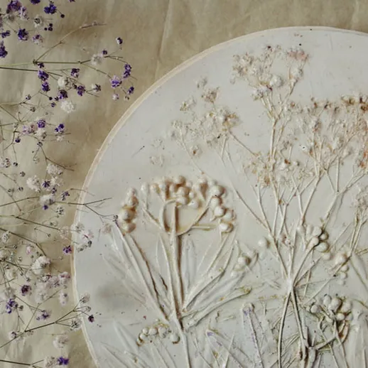 Ручная работа с прессованными цветами и глиняной рельефной панелью в мастерской на фоне нейтральной ткани