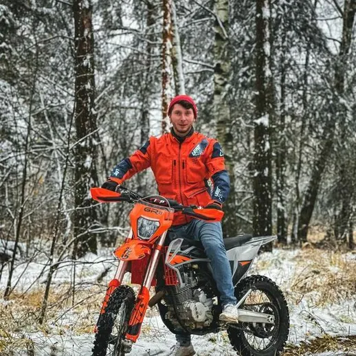 Молодой человек на мотоцикле в зимнем лесу, окруженном снегом, наслаждается ездой в морозный день