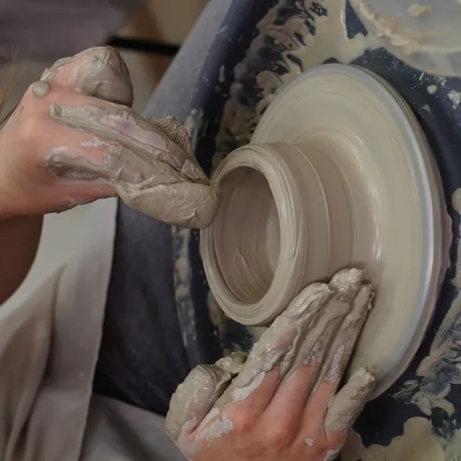 Создание керамического изделия на гончарном круге в мастерской, где мастер работает с глиной и формирует сосуд