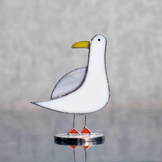 Стеклянная фигурка птицы на отражающей поверхности в светлом помещении