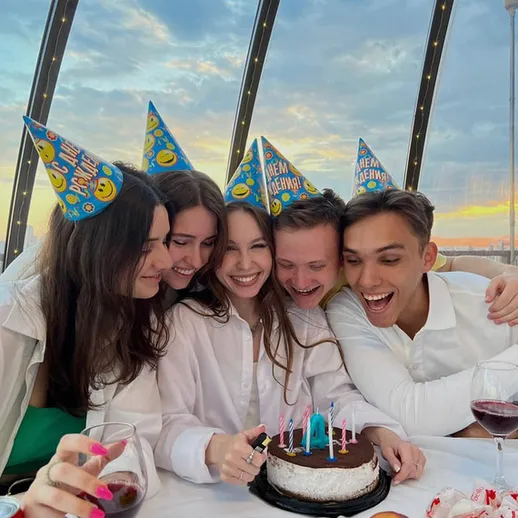 Друзья отмечают день рождения девушки на крыше с восхитительным видом, наслаждаясь тортом в солнечное время