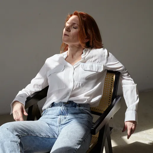 Женщина в белой рубашке и джинсах relaxs на стуле в светлом интерьере на фоне мягкого солнечного света