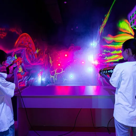 Взрослые развлекаются в помещении с неоновыми световыми эффектами и граффити, играя в лазертаг