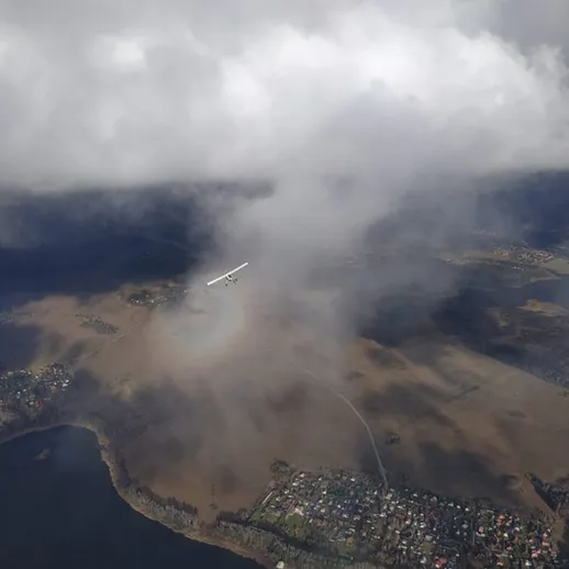 Самолет в облаках над озером и прибрежным селом, запечатлен зимой с высоты