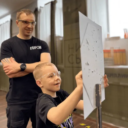 Мальчик стреляет по мишени на тренировке под руководством инструктора в спортивном зале