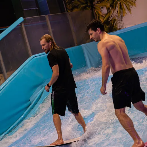 Два серфера качаются на искусственных волнах в закрытом аквапарке ночью