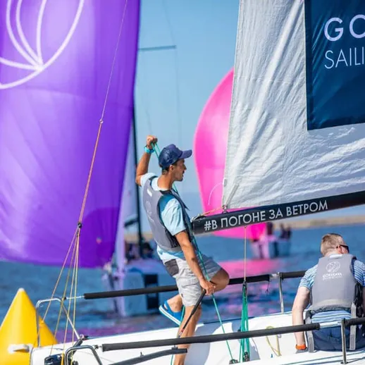 Участники парусной регаты на фоне ярких парусов в солнечный день на водоёме